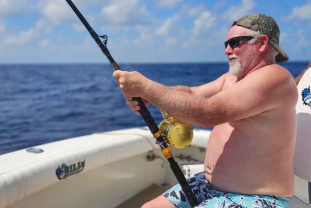 man holding rod reeling in fish on 4 hr deep sea fishing charter in cancun mexico