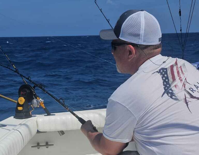man holding rod reeling in fish while on 8 hr deep sea fishing charter boat in mexico