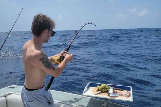 man using live bait on back end of big game fishing charter boat to cast line
