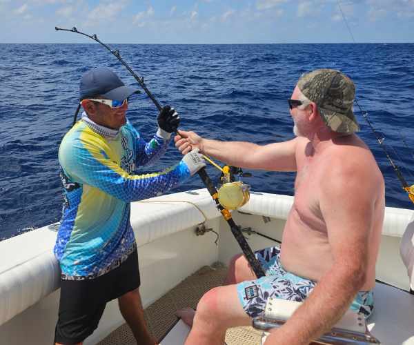 captain showing man how to use new rod on cancun charter fishing boat